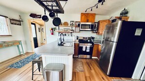 A kitchen with wooden cabinets, a stainless steel refrigerator, and a central island with a trash can.