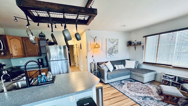A modern kitchen with a central island, bar stools, a refrigerator, and hanging pots.