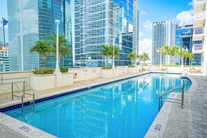 Una piscina con una profondità massima di 1,5 metri, circondata da palme e moderni grattacieli.