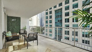 A balcony with a view of tall buildings, a green wall with the word "Miami," and a seating area with chairs and a bench. - Zeus Sanctuary in Brickell Miami (Miami)