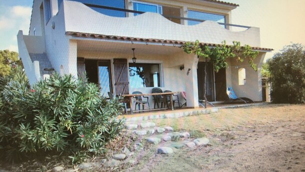 A two-story house with a patio, outdoor seating, and a garden. - Home. (Zonza)