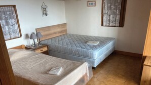 A bedroom with two beds, a nightstand with a lamp, and a wooden headboard. - Home. (Zonza)