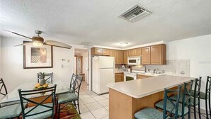 A modern kitchen with a central island, wooden cabinets, and a dining area with chairs. - Kick back and Relax at Leisure Beach (Hudson)