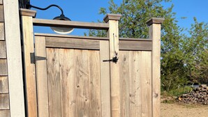 Une porte en bois, munie d’un loquet, est installée dans un espace recouvert de gravier, avec des arbres en arrière-plan.