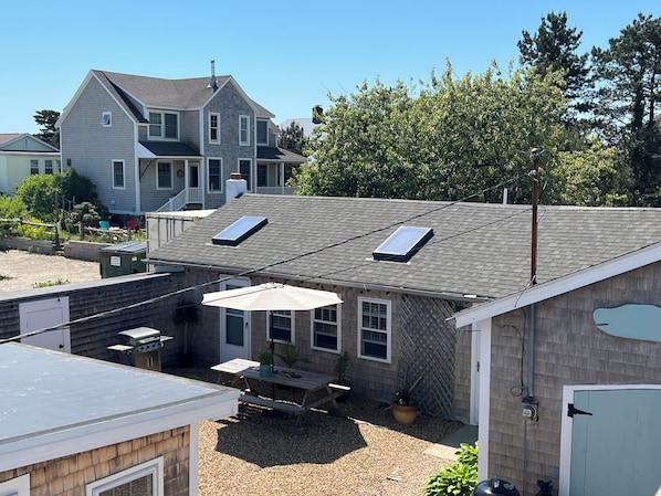 A residential building with a sloped roof, two skylights, a patio area with a table and chairs, and a small garden.