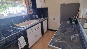 A kitchen with a gas stove, a sink, a microwave, and a cabinet. There are hanging lights and a window with curtains.