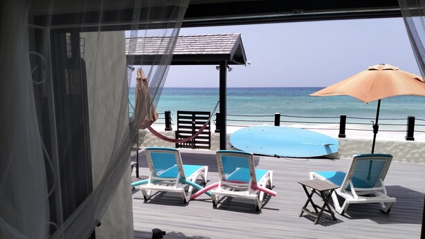 A beachside deck with lounge chairs, a blue surfboard, and a beach umbrella.