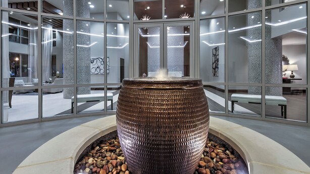 Een moderne lobby met een groot, reliëf waterkunstwerk in het midden, omringd door zitgedeeltes en glazen scheidingswanden.