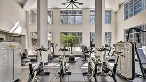Een sportschool met diverse fitnessapparaten, grote ramen en een modern plafond.