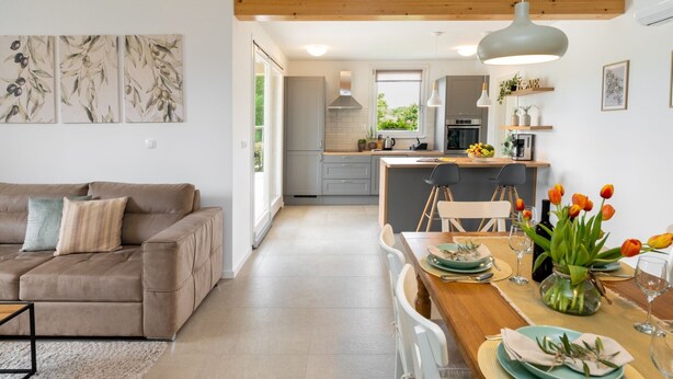 A modern kitchen with a central island, a dining area with a table set for two, and a living room with a sofa and a coffee table. - Holiday Home Olea - 3 Bedrooms (Labin)