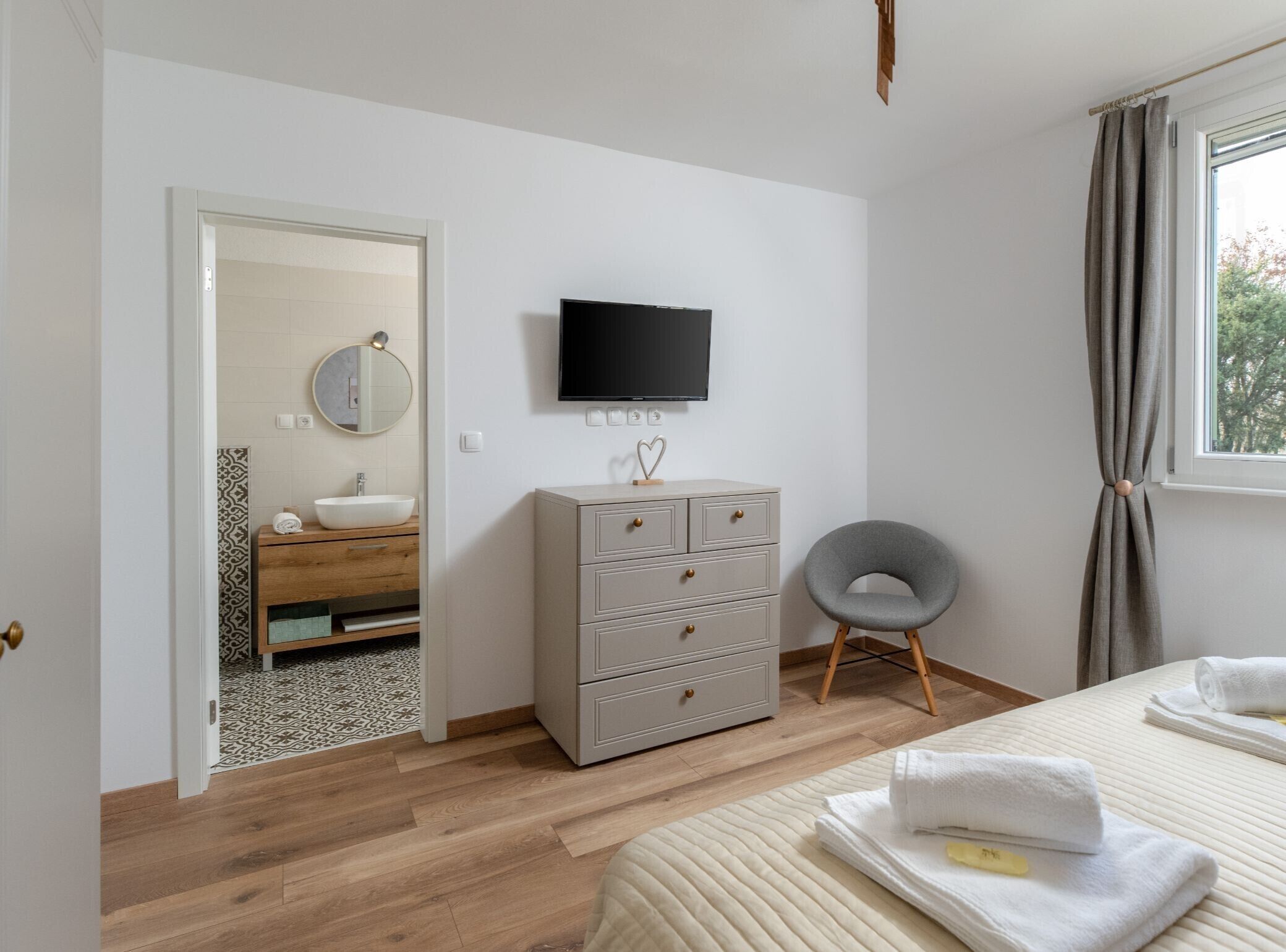 Ein Schlafzimmer mit Bett, Schminktisch, Fernseher und einem durch eine offene Tür einsehbaren Badezimmer.