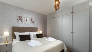 A neatly made bed with white linens and two pillows, a bedside table with a lamp, and a wardrobe with a mirror. - Holiday Home Olea - 3 Bedrooms (Labin)