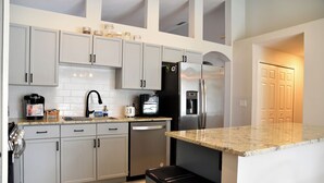 Una cocina moderna con armarios blancos, un refrigerador de acero inoxidable, una cafetera y un lavavajillas.