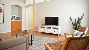 Una sala de estar moderna con un televisor de pantalla plana, muebles de madera y una planta grande.