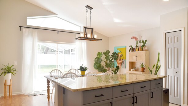 Una cocina con una isla grande, armarios blancos y una variedad de plantas.