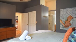 Un dormitorio con una cama grande, un aparador, un televisor y una puerta que da a otra habitación.