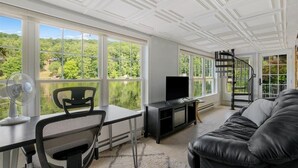 Un salon moderne doté d’une grande fenêtre, d’un canapé en cuir noir, d’un téléviseur posé sur un meuble noir et d’un escalier en colimaçon noir.