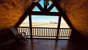 A wooden cabin with a balcony, a rocking chair, and a view of a distant landscape.