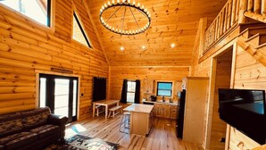 A log cabin interior with a living room, kitchen, and dining area.