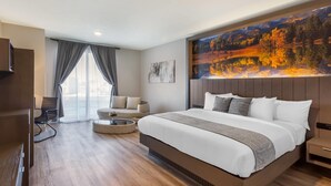 A modern hotel room with a large bed, a sofa, a TV, and a painting on the wall.
