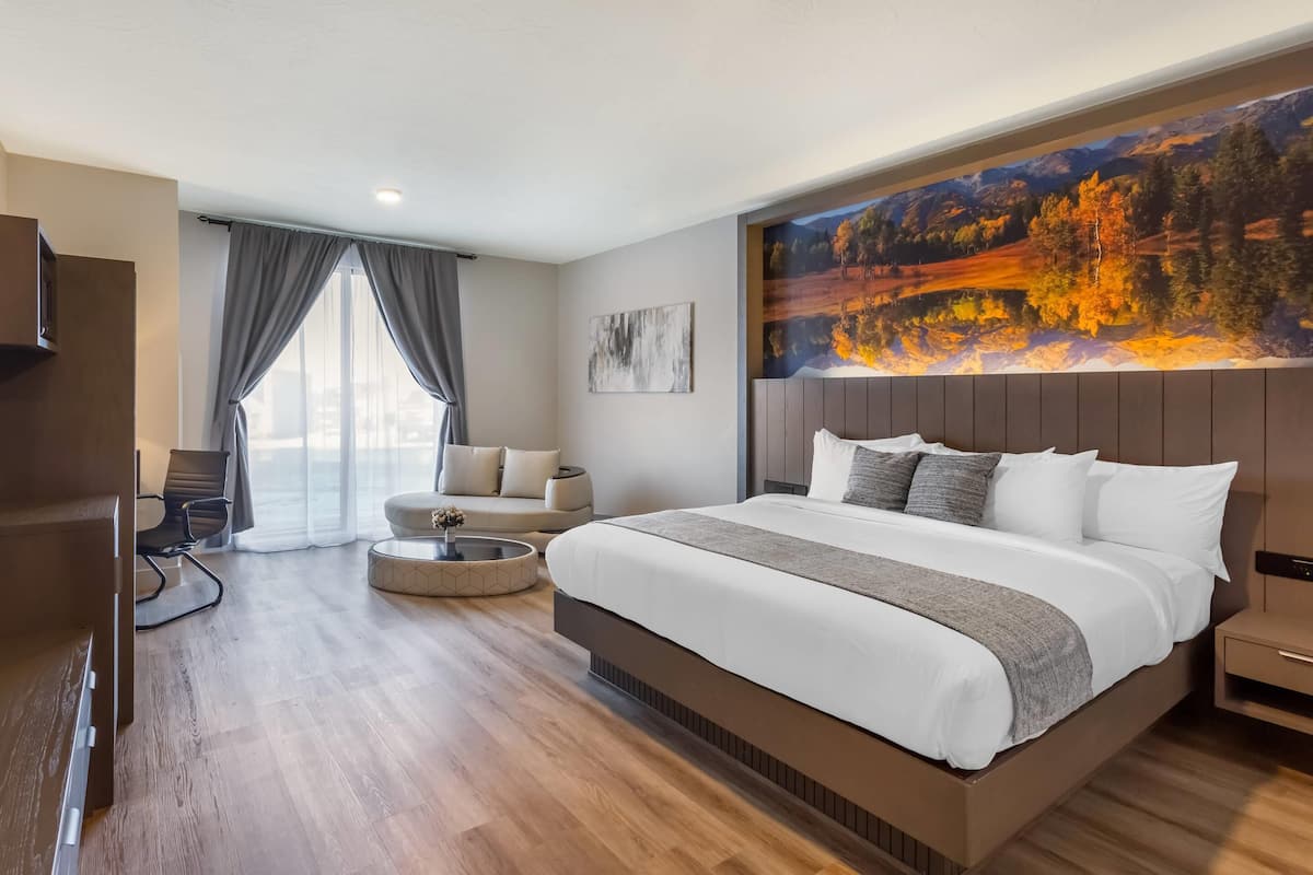 A modern hotel room with a large bed, a sofa, a TV, and a painting on the wall.