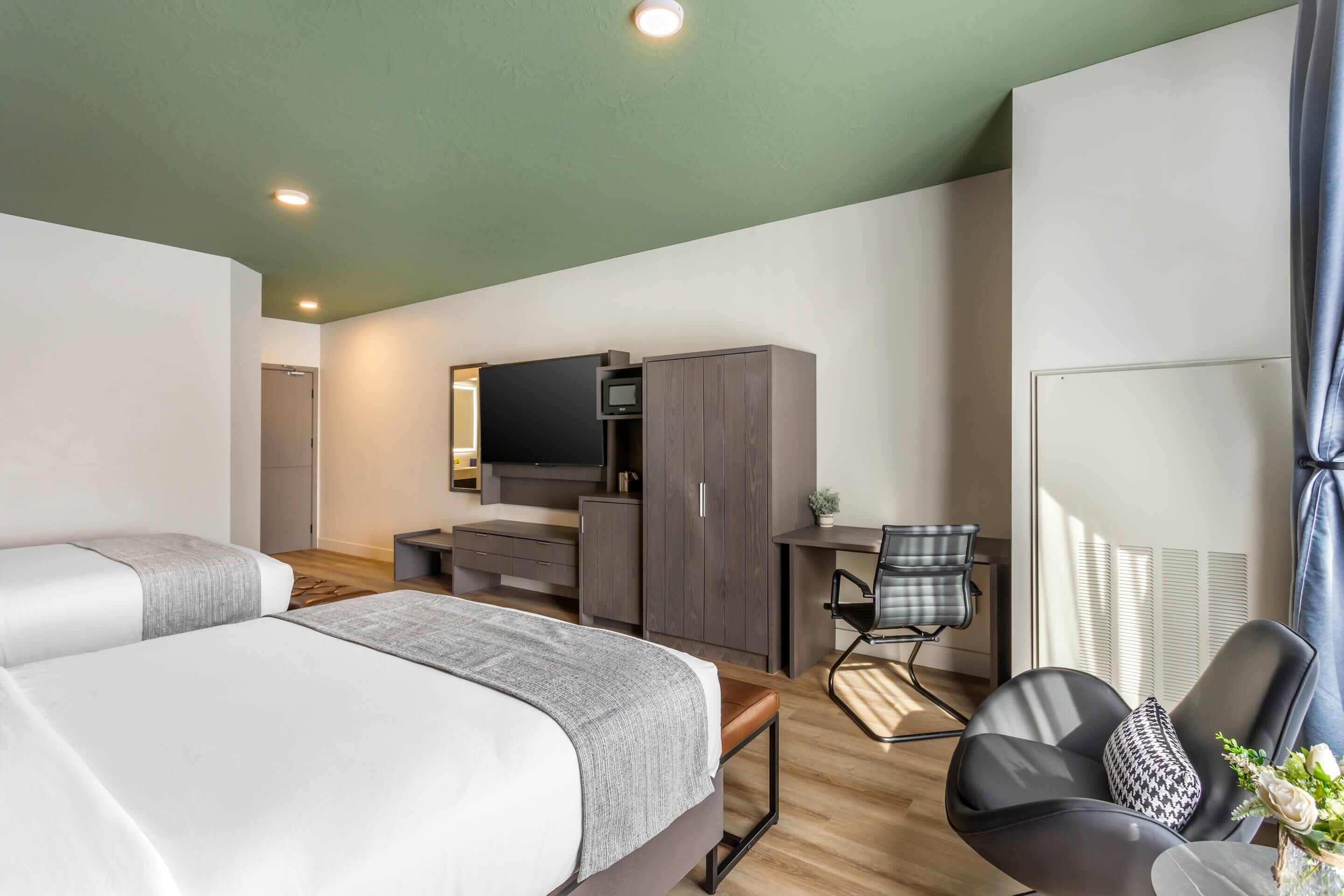 A hotel room with two beds, a desk, a chair, a TV, and a wardrobe.