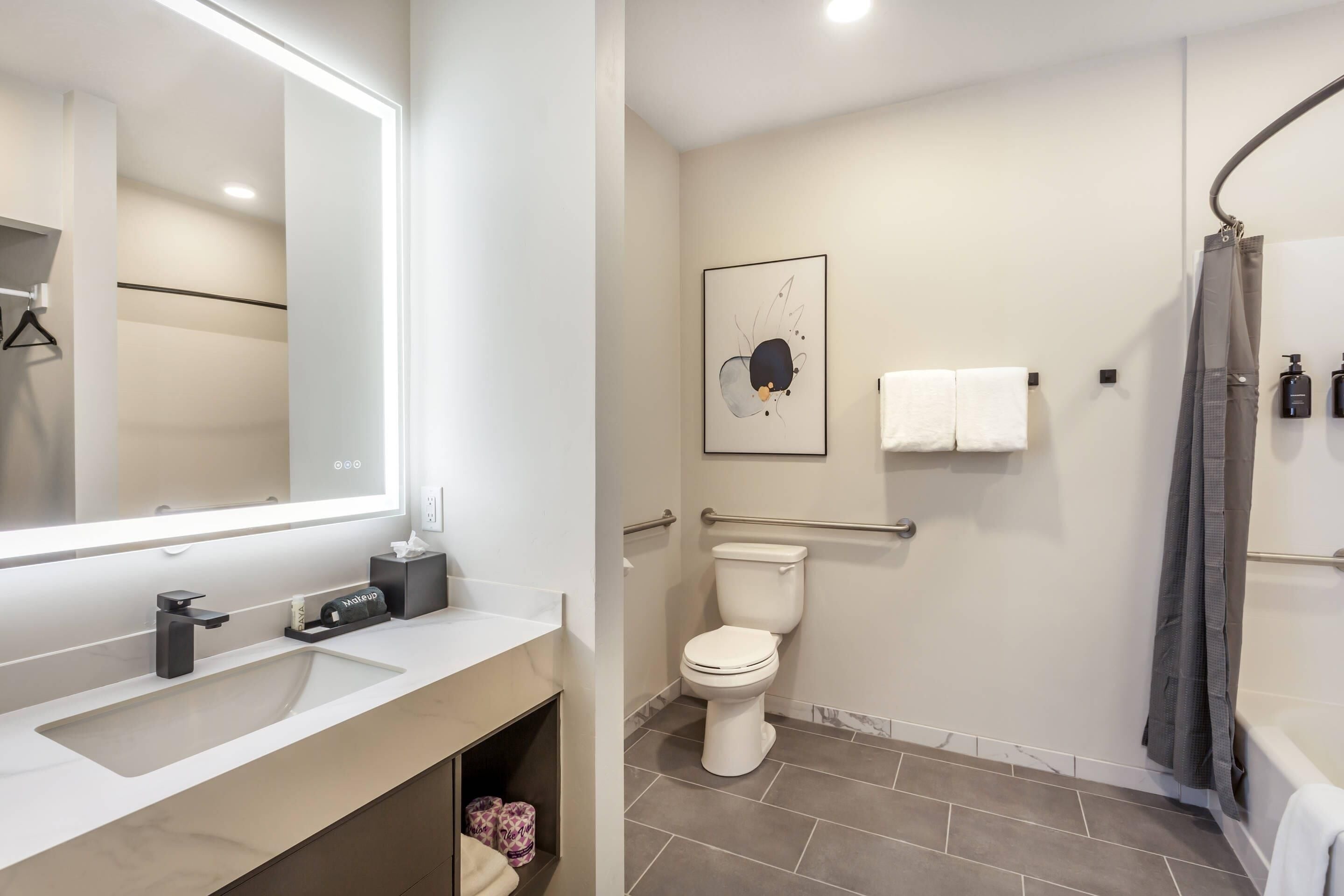 A modern bathroom with a large mirror, a toilet, a shower, and a sink.