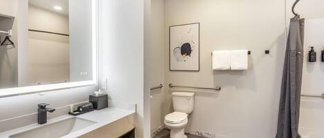 A modern bathroom with a large mirror, a toilet, a shower, and a sink.