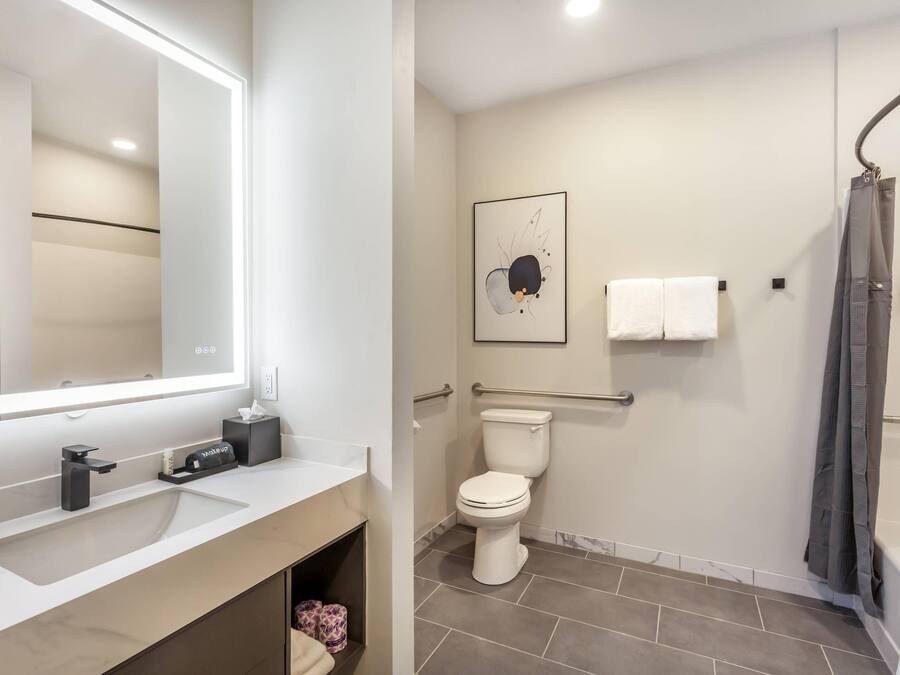Un baño moderno con un espejo grande, un inodoro, una ducha y un lavabo.