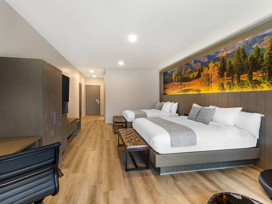 Una habitación de hotel moderna con una cama grande, un escritorio, un banco y un televisor.