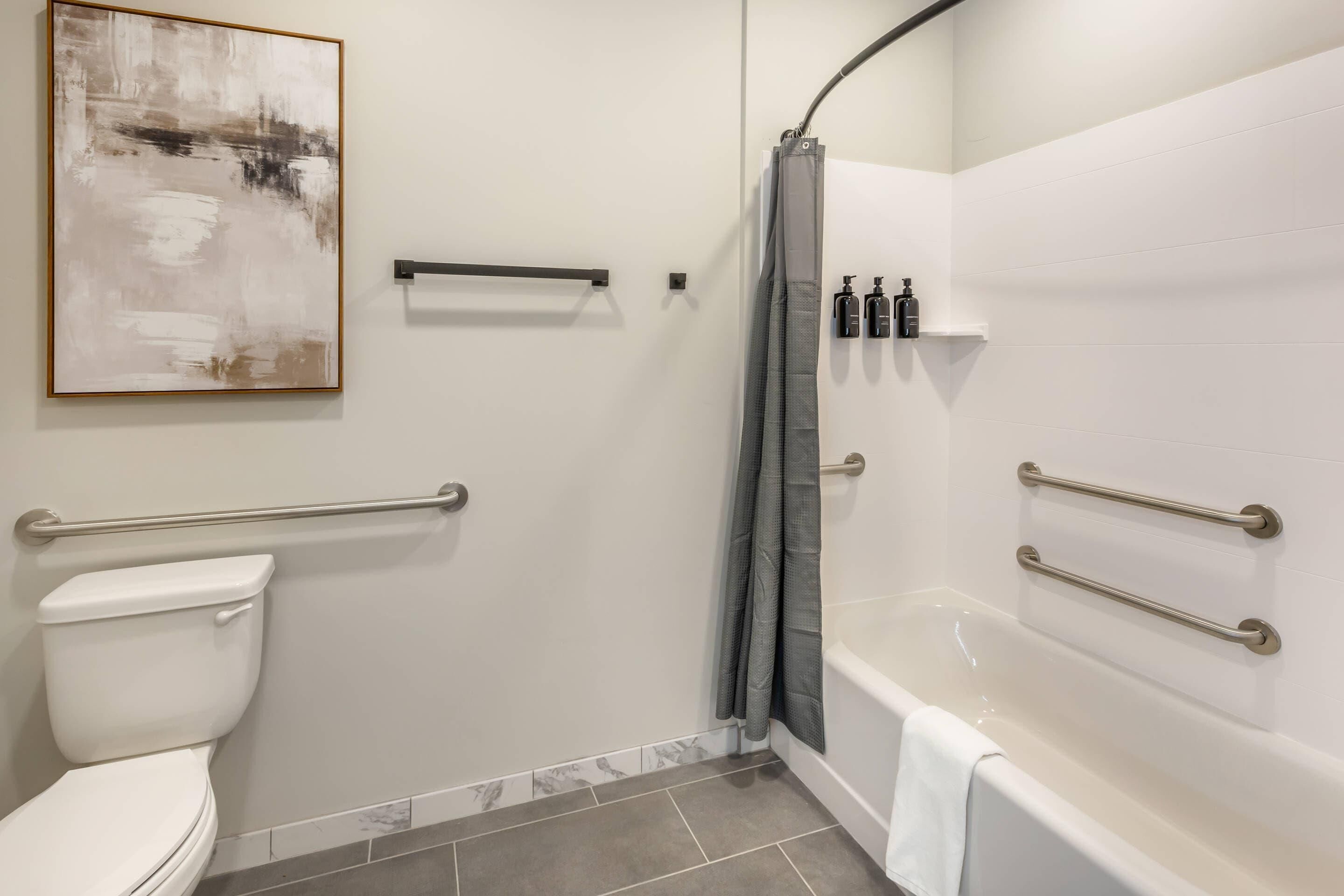 Un baño moderno con inodoro, ducha y bañera. Incluye barras de apoyo, un perchero y una cortina de ducha.