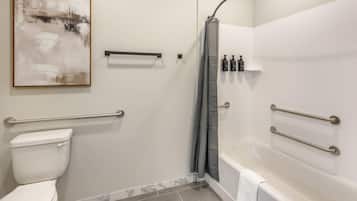 Een moderne badkamer met toilet, douche en bad. Er zijn handgrepen, een handdoekrek en een douchegordijn aanwezig.
