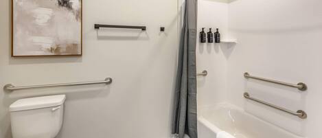 A modern bathroom with a toilet, shower, and bathtub. It includes grab bars, a towel rack, and a shower curtain.