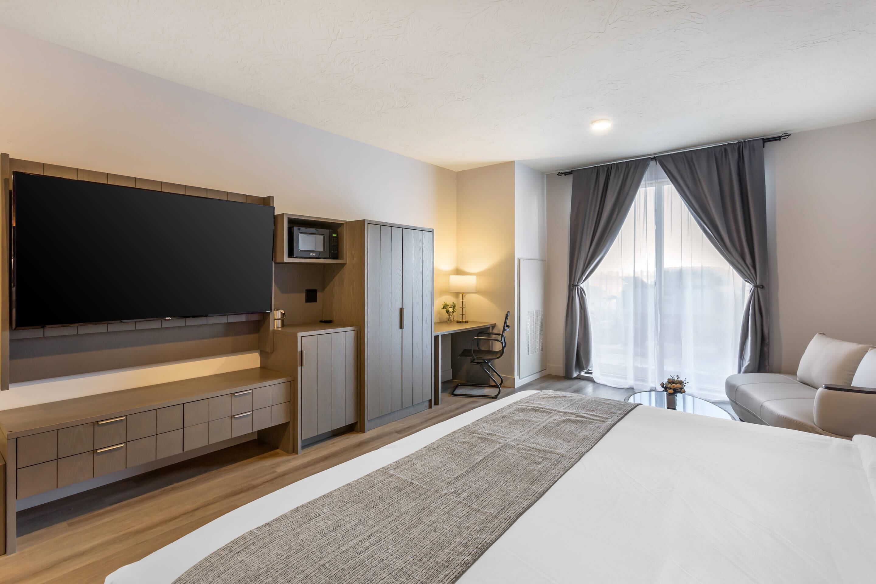 Una habitación de hotel moderna con una cama grande, un televisor de pantalla plana, un escritorio con una silla y un sofá.