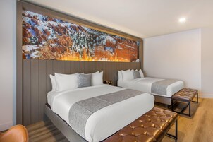 Habitación de hotel con dos camas, un mural grande en la pared y un banco de madera.