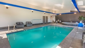 A swimming pool with a blue border, a hot tub, and a seating area with cushions.