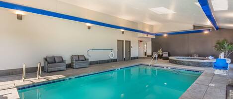 A swimming pool with a blue border, a hot tub, and a seating area with cushions.