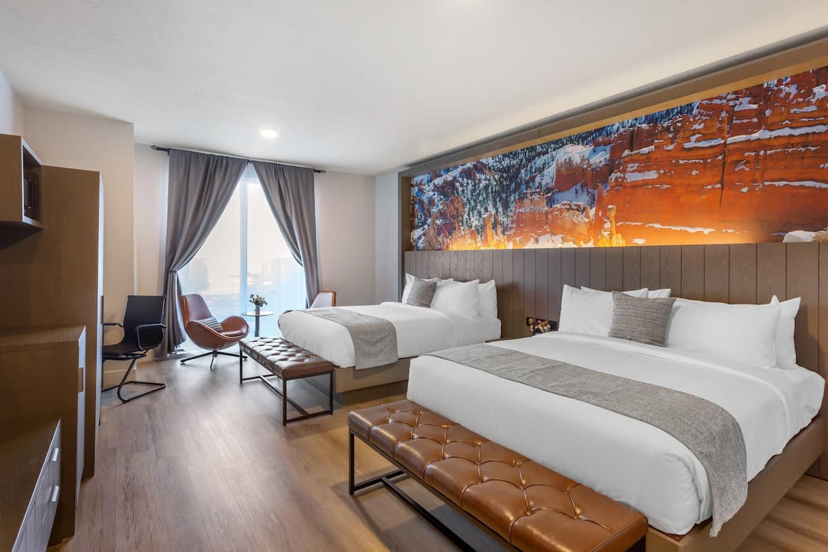 A hotel room with two beds, a large painting, a desk, and a chair.