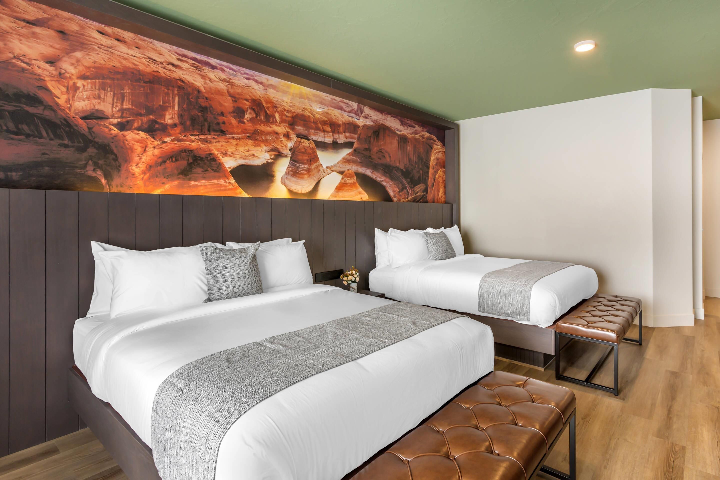 A hotel room with a large bed, a smaller bed, and a bench.