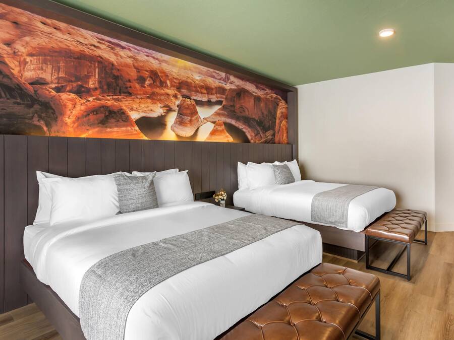 A hotel room with a large bed, a smaller bed, and a bench.