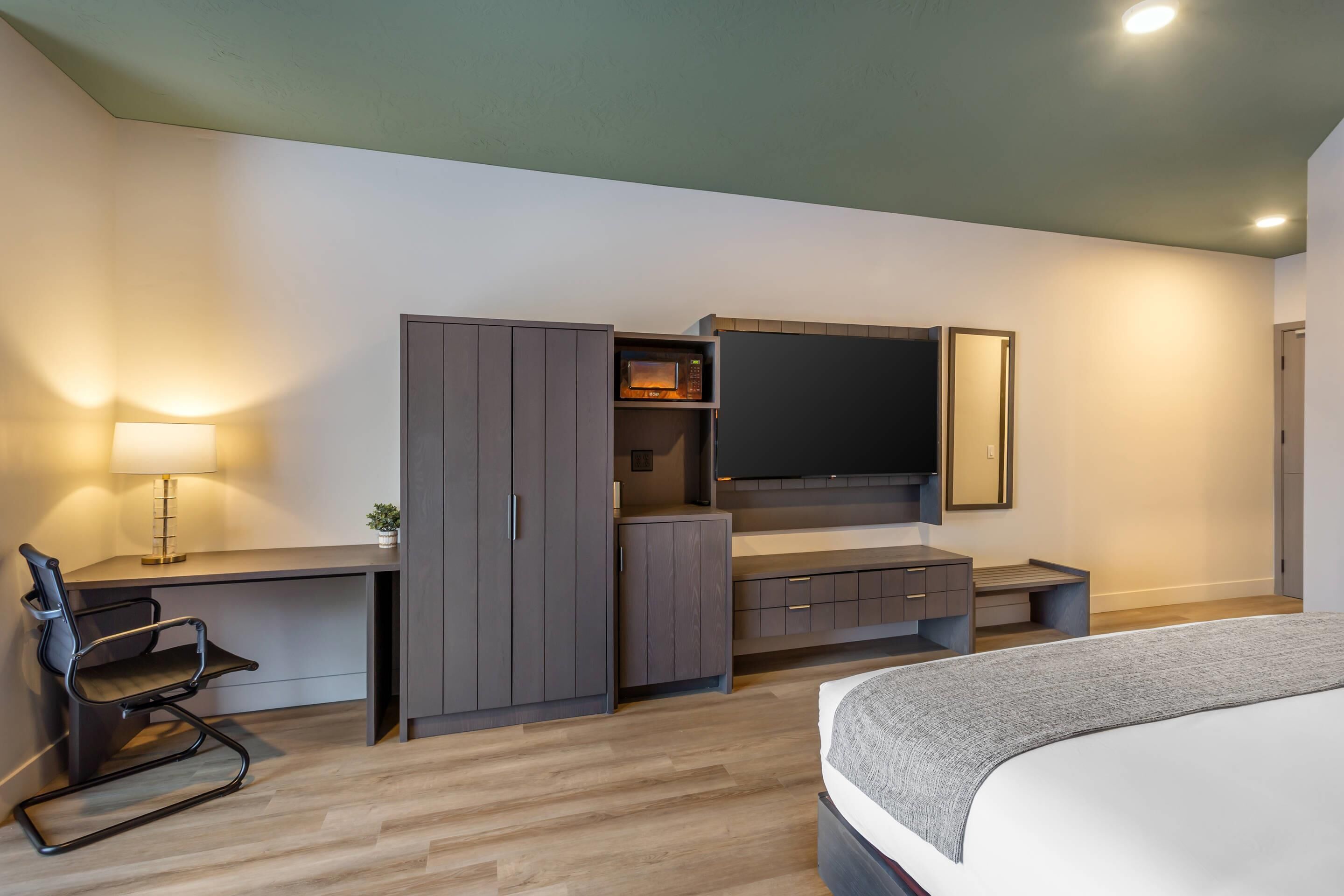 Um quarto moderno com cama, escrivaninha, cadeira, televisão e guarda-roupa.