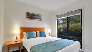 Une chambre d’hôtel avec un lit, deux lampes de chevet, une table de nuit, un tableau encadré au mur et une grande fenêtre donnant sur un paysage verdoyant.