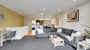 Un appartement moderne avec un canapé gris, un coin repas et une cuisine en arrière-plan.