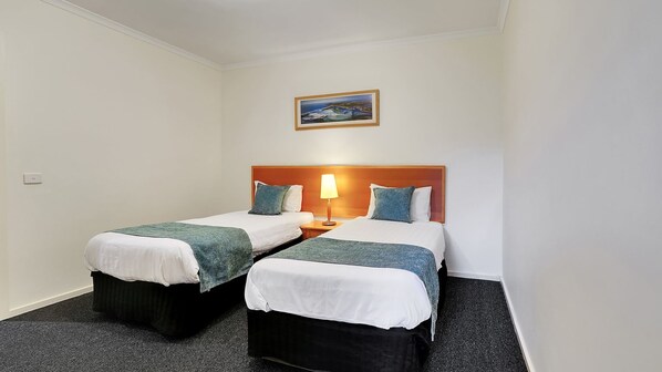 Une chambre d’hôtel avec deux lits simples, une table de chevet avec une lampe, un tableau au mur et un sol recouvert de moquette.