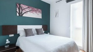 Un dormitorio moderno con una cama grande, una mesita de noche, una lámpara de pared y una ventana con cortinas.