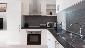 Una cocina moderna con armarios blancos, horno empotrado, microondas y pileta de acero inoxidable.