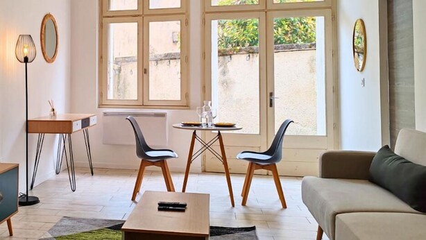 A modern living room with a sofa, two chairs, a coffee table, a small table with a lamp, and a window with a view of greenery. - Chill and Work  (Villeneuve-sur-Lot)