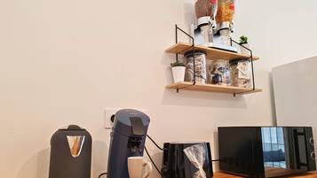A kitchen with a coffee maker, a microwave, a toaster, and a shelf with jars and a potted plant.