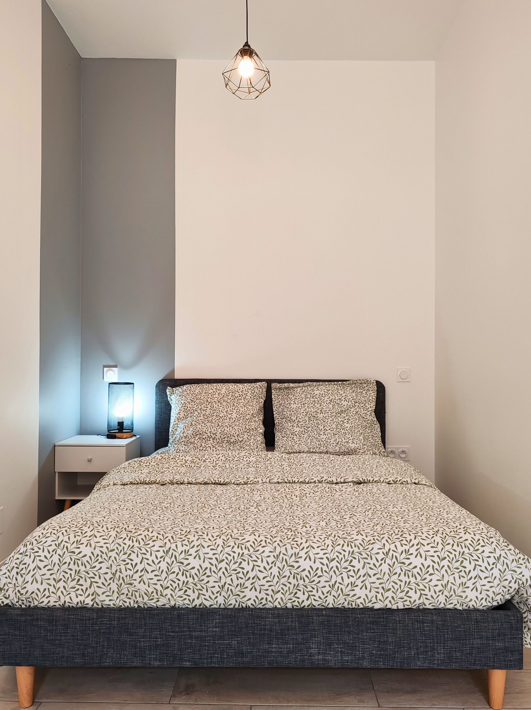 A bedroom with a bed, a nightstand, a lamp, and a hanging light fixture.