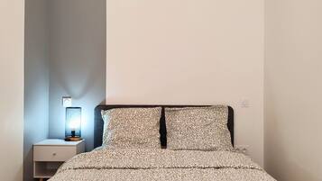 A bedroom with a bed, a nightstand, a lamp, and a hanging light fixture.